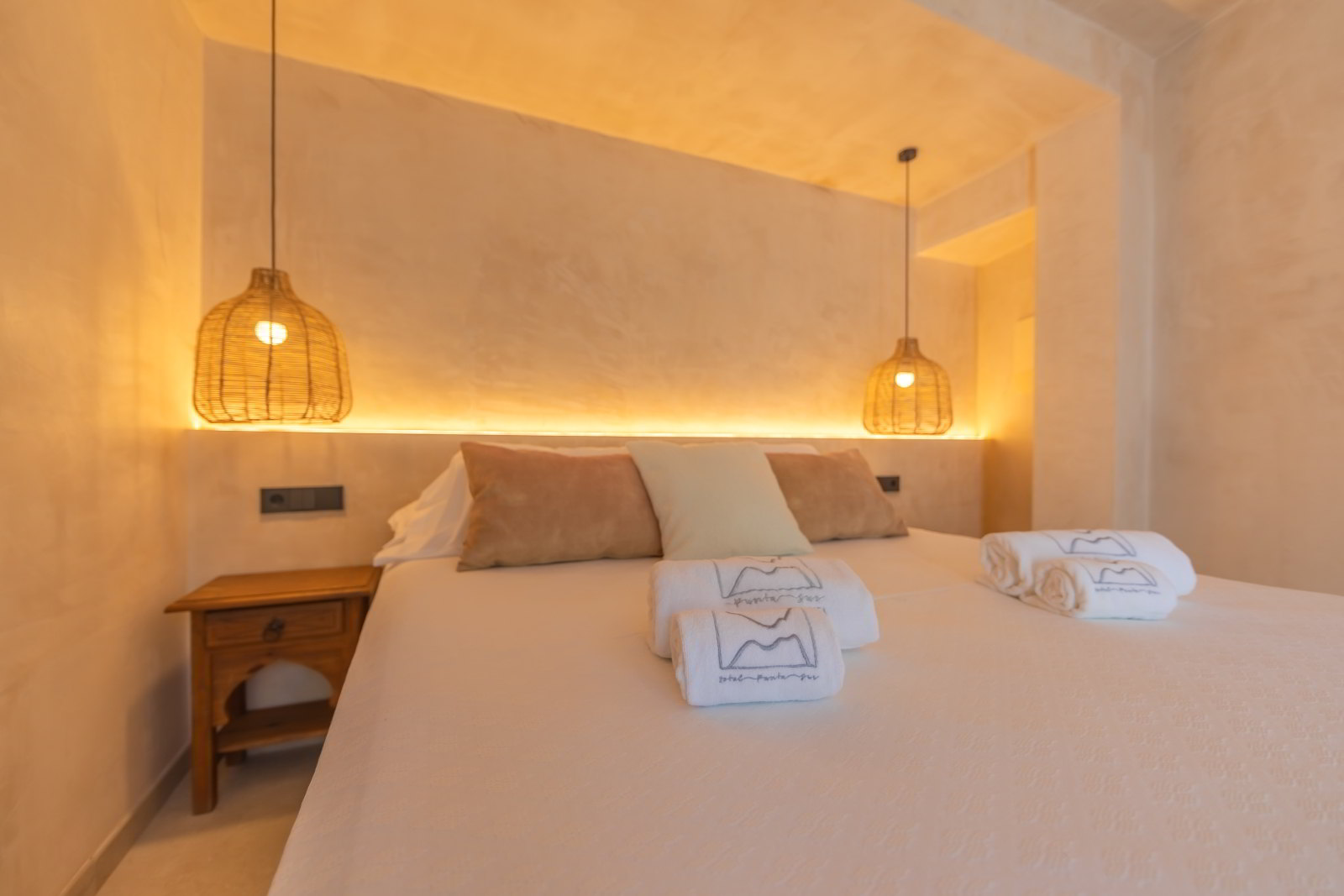 Cama doble en La Villa del Hotel Punta Sur con iluminación cálida, cojines en tonos neutros y lámparas de mimbre colgantes.