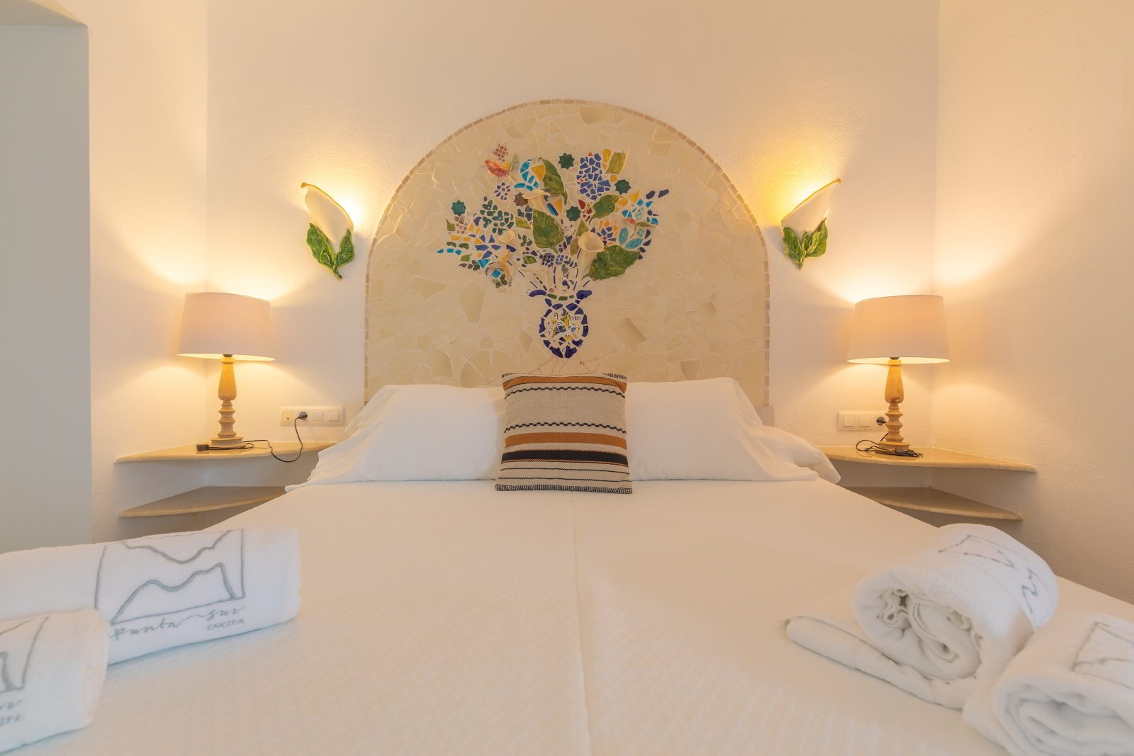 Dormitorio principal de una Habitación Junior Suite con cama doble, iluminación cálida, cabecero decorativo artesanal y ambiente acogedor.